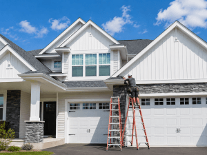 Worker on ladders performing gutter maintenance on a large modern suburban home.